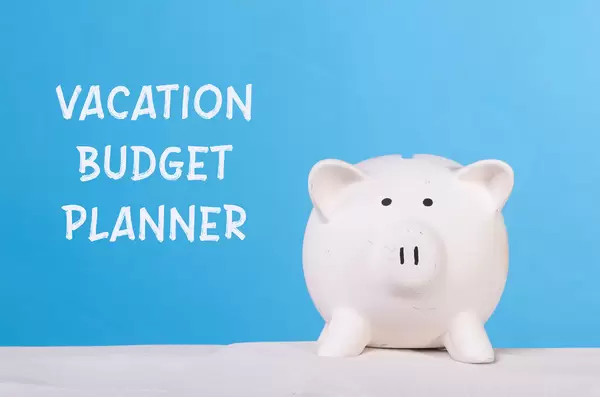 Piggy bank on sandy beach with Vacation budget planner text