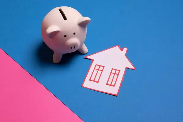 Piggy bank with house made out of paper on blue background