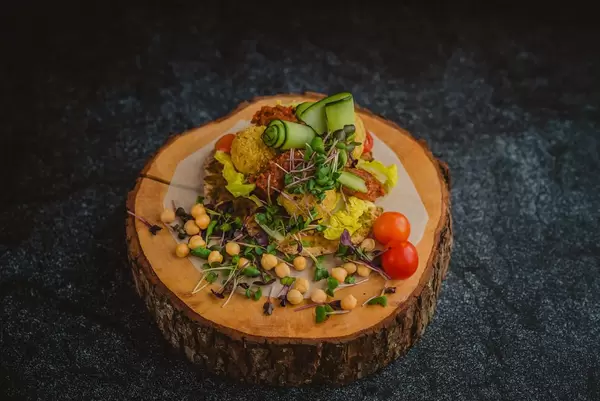 Pikante Hähnchen und Pesto-Bällchen mit allerlei farbenfroher Garnierung präsentiert auf Baumstammscheibe - frontale Nahansicht