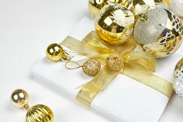 Pile of golden Christmas tree ornaments and present box wrapped in white paper