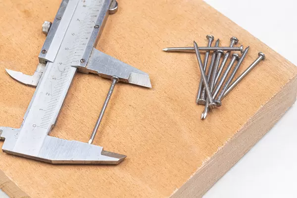 Pile of Nails on the wooden board with measuring caliper
