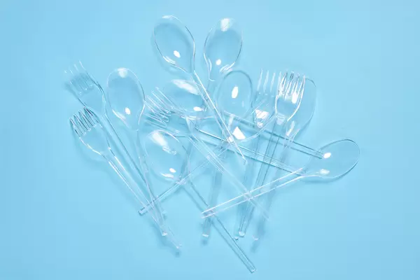Pile of plastic spoons and forks on blue background