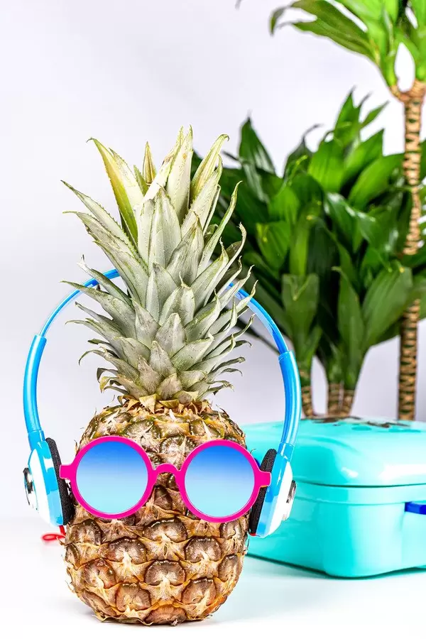 Pineapple in sunglasses and headphones with a suitcase and palm trees in the background