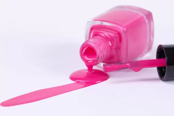 Pink nail polish spilled from the bottle with brush on white background