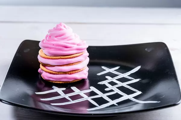 Pinker Nachtisch mit farbiger Sahne auf einem schwarzen, verzierten Teller