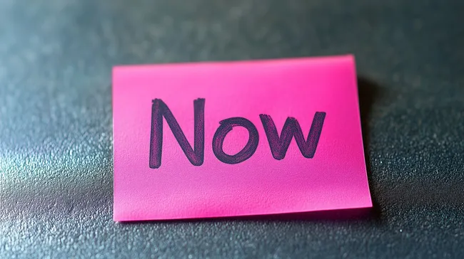 Pinkes Post-it-Zettel mit Aufschrift 'Now' auf glänzender Oberfläche
