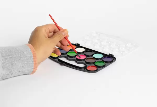 Pinsel in der Hand einer jungen Frau und Wasserfarben