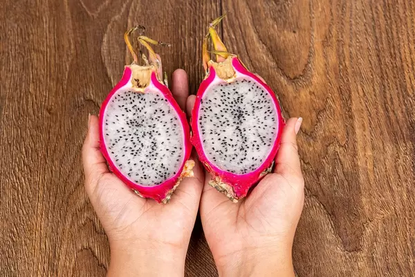 Pitahaya fruit halves in female hands on a wooden background, top view