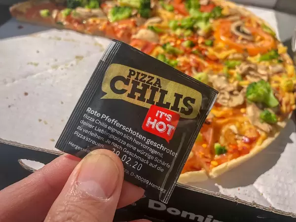 Pizza Chilis from Dominos with crushed red peppers and vegan Kap Verde Pizza in the background