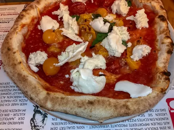 Pizza in restaurant with thick crispy edge, tomatoes and unmelted mozzarella cheese