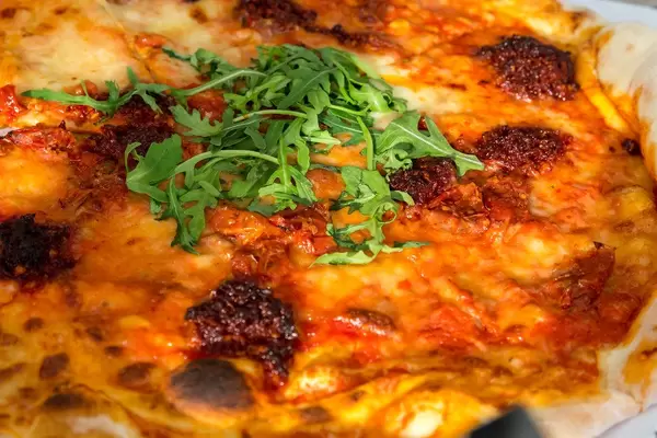 Pizza NDUJA CALABRESE in the L'Osteria with mozzarella, Italian salami spread, semi-dried cherry tomatoes and rucola