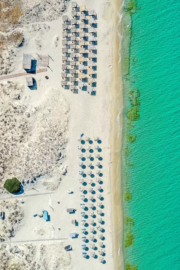 Plaka, Naxos. Drei Reihen runder Sonnenschirme aus Stroh und vier Reihen quadratischer Sonnenschirme