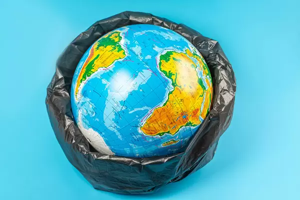 Planet earth in plastic bag on blue background. Concept - ecology, planet pollution with plastic cellophane polyethylene earth day, world environment day
