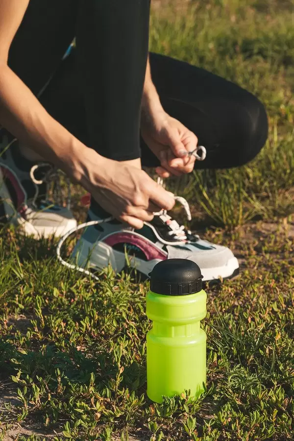 Plastic water bottle on the grass and female athlete preparing for jogging outdoors. Sport active lifestyle concept