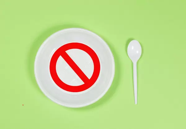 Plastik verboten - Einweg-Plastikteller und Löffel auf grünem Hintergrund