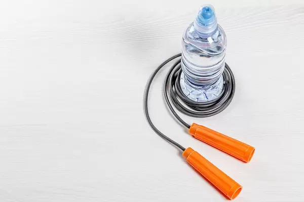 Plastik Wasserflasche und Sprungseil auf weißem Holzuntergrund als Symbolik für einen aktiven Lebensstil