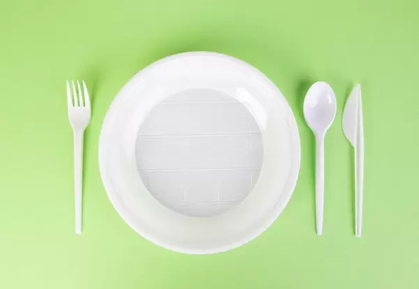 Plastikgeschirr mit Teller und Besteck für Einmalverwendung vor grünem Hintergrund