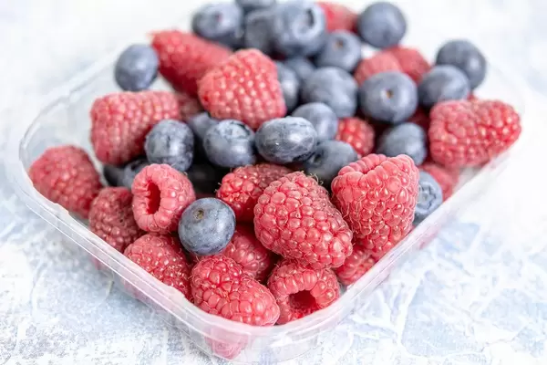 Plastikschale gefüllt mit leckeren frischen Himbeeren und Blaubeeren auf Marmortisch