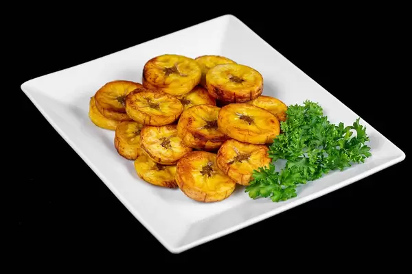 Plate with fried plantain and herbs on a black background