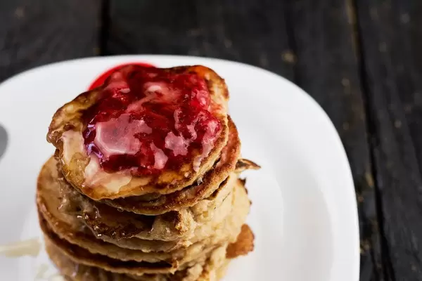 Plate with pancakes and strawberry jam on dark wood background