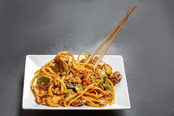 Plate with rice noodles and chopsticks on black background
