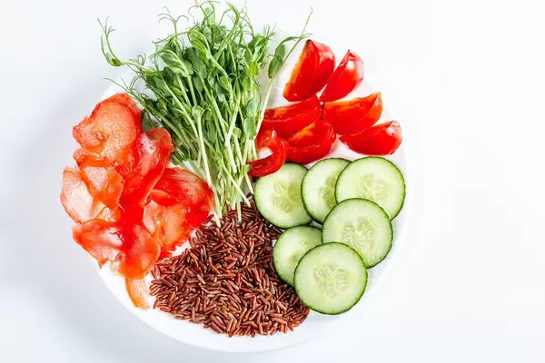 Plate with slices of tomato, cucumber, pickled ginger, brown rice and micro-green peas. Top view