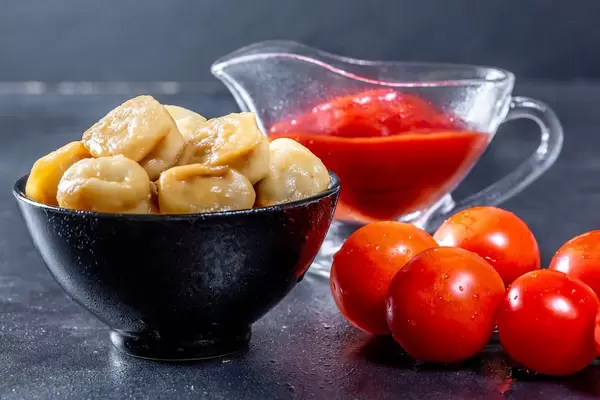 Plate with tasty dumplings and sauce on black background