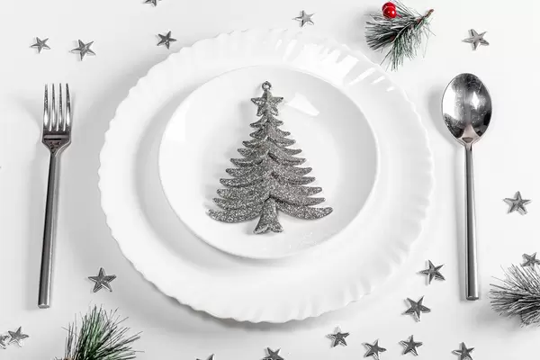 Plates with spoon and fork on a white table with Christmas silvery decor