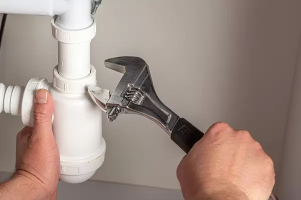 Plumber with adjustable wrench repairing pipes
