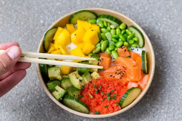Poké bowl salmon: rice bowl with mango, masago, soybeans, vegetables. Eating with chopsticks