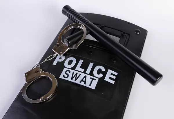 Police shield with handcuffs and rubber baton on white background