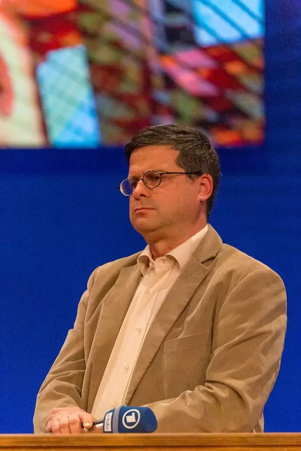 Political scientist Prof. Gideon Botsch standing at the wooden desk in front of a blue background, at the stage for the German ARD magazine "Kontraste"