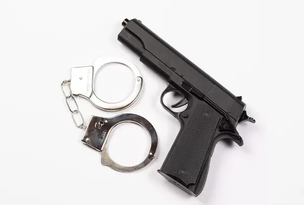 Polizei-Ausrüstung - Schwarze Handfeuerwaffe neben Handschellen vor weißem Hintergrund