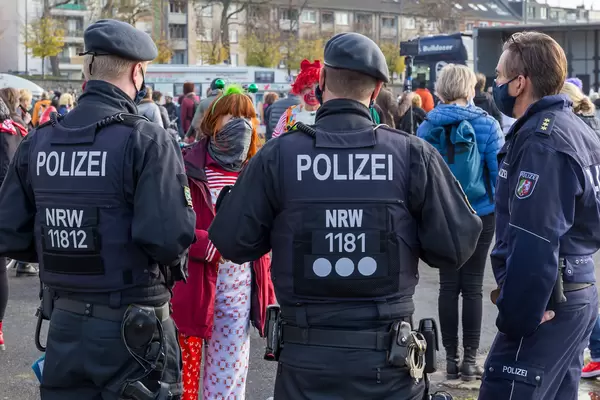 Polizisten reden mit einer Frau mit Halstuch als Mundschutz, in traditionellen Farben von Köln verkleidet