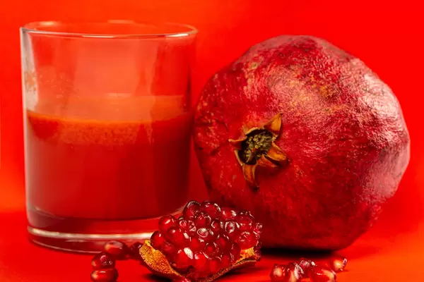 Pomegranate juice with fresh pomegranate on a red background
