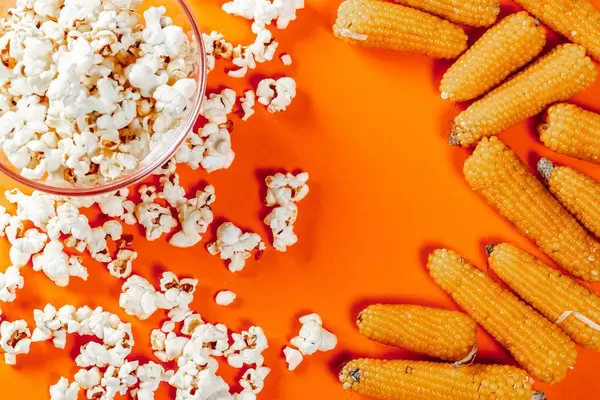Popcorn and raw corn on orange background