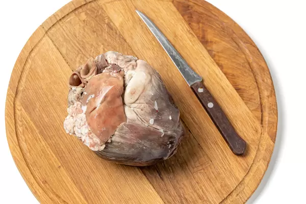 Pork cooked heart on a wooden kitchen board with a knife, top view