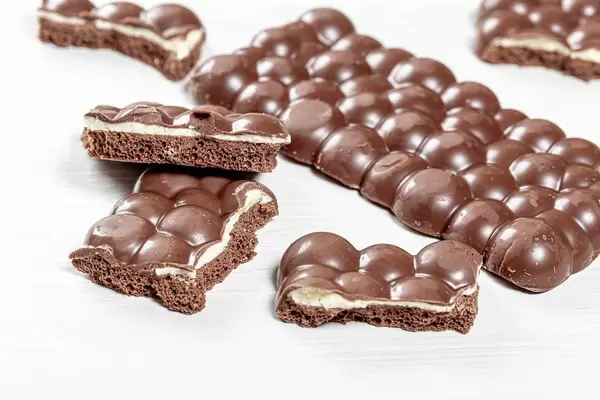 Porous milk with white chocolate whole and pieces on white wooden background