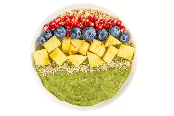 Porridge with blueberries, pomegranate, pineapple pieces, sesame seeds and green fruit puree on white, top view
