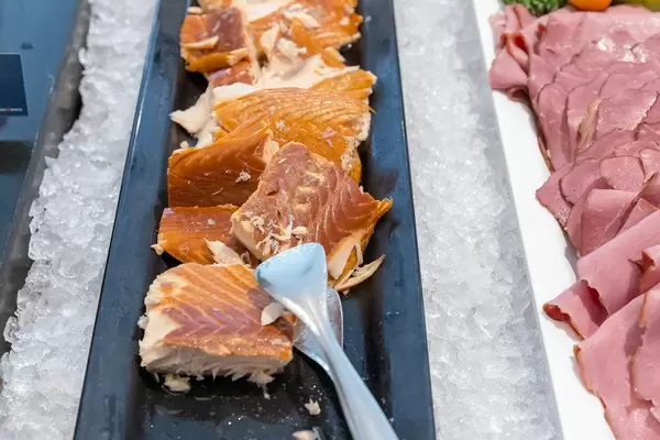 Portionierter Fisch am Hotelbüfett, für ein ausgewogenes Essen, angerichtet auf einem schwarzen Tablett und auf Eiswürfeln gekühlt