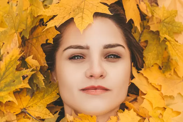 Portrait of a beautiful girl with makeup and yellow maple leaves around her face
