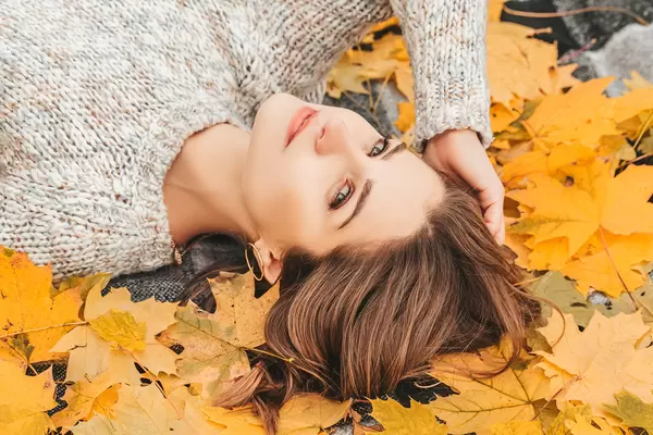 Portrait of a beautiful happy woman with a smile with an autumn yellow leaf in the park