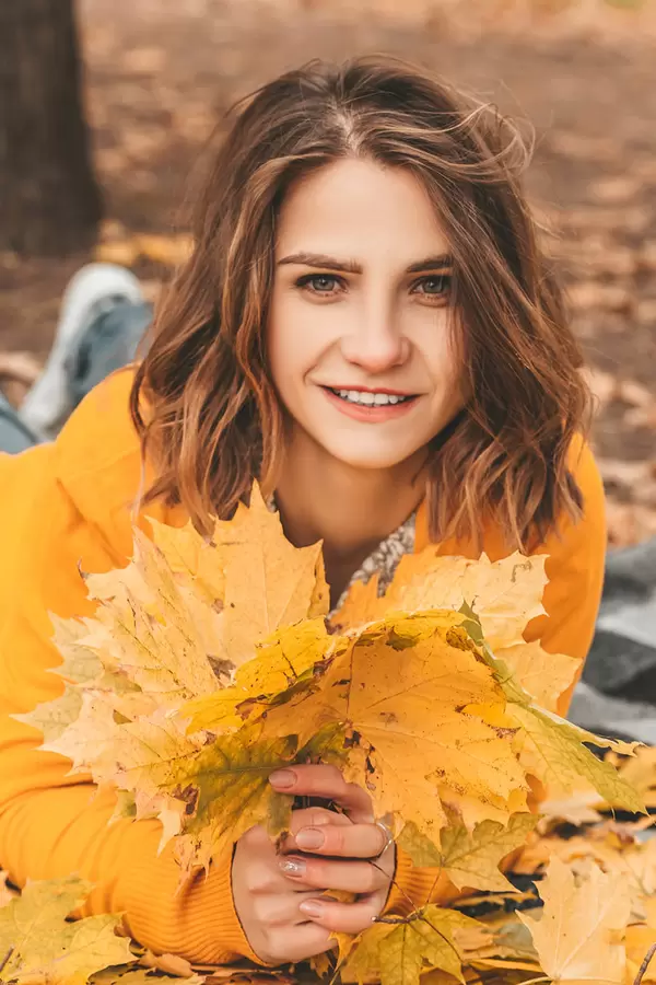 Portrait of a beautiful happy woman with a smile with an autumn yellow leaves in the park