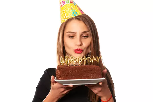 Portrait of beautiful girl wearing cone cap holding birthday cake with candles and making a wish