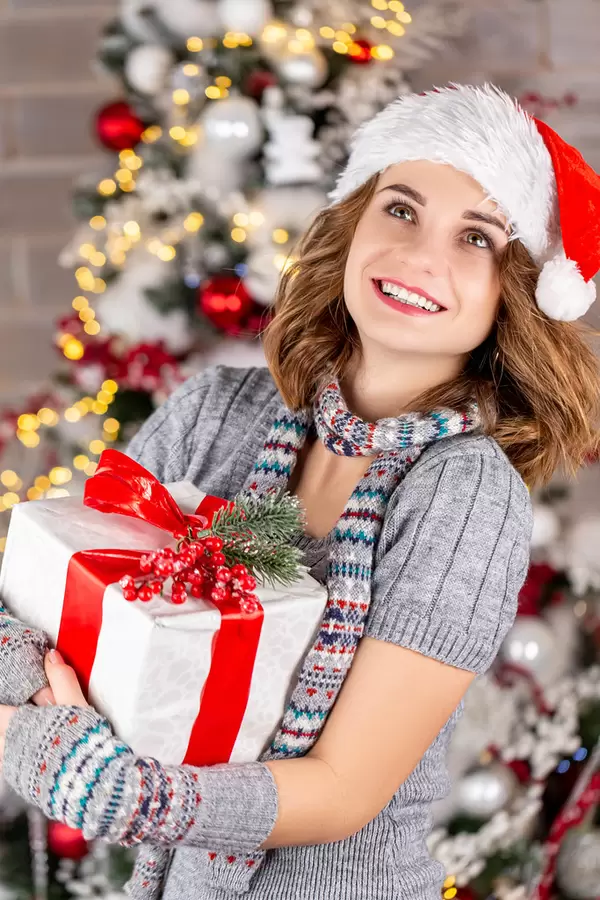 Portrait of happy girl with gifts near a christmas tree in the santa hat