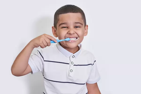 Portrait of little boy brushing teeth on light background