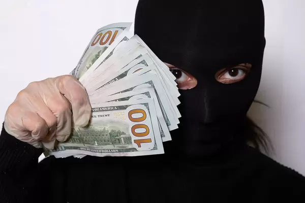 Portrait shot of a thief woman in black face mask holding a pile of stolen US dollars