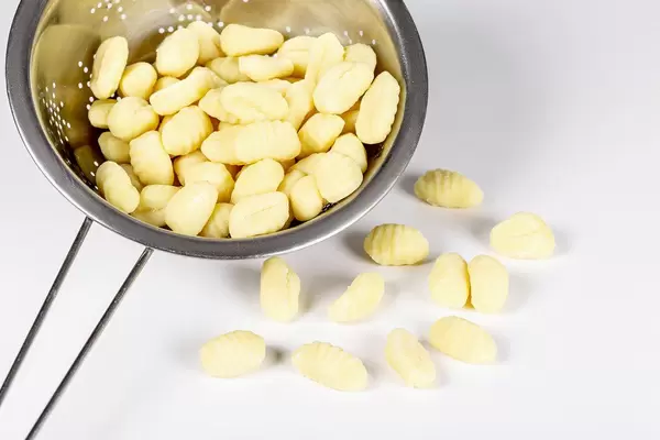 Potato gnocchi in colander on white background