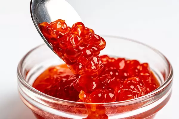 Pour red caviar into a glass bowl, close-up