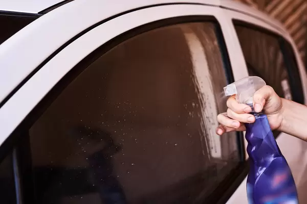 Pouring glass cleaning spray on car side window surface